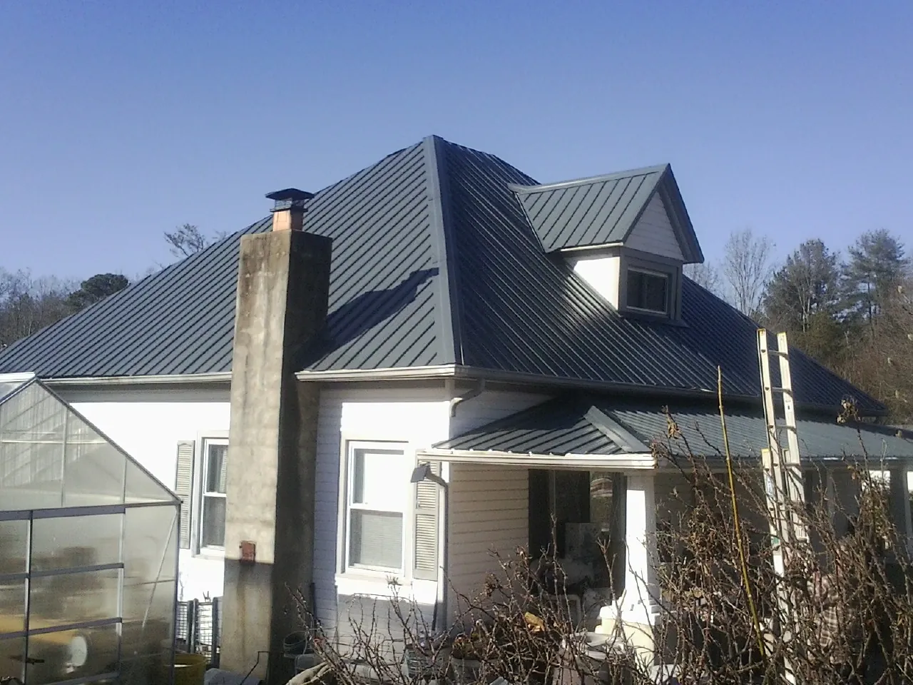 Dark blue standing seam metal roof on a white farmhouse with dormer — Slate & Tile Roof Repair by Roofing Brothers in Royalston