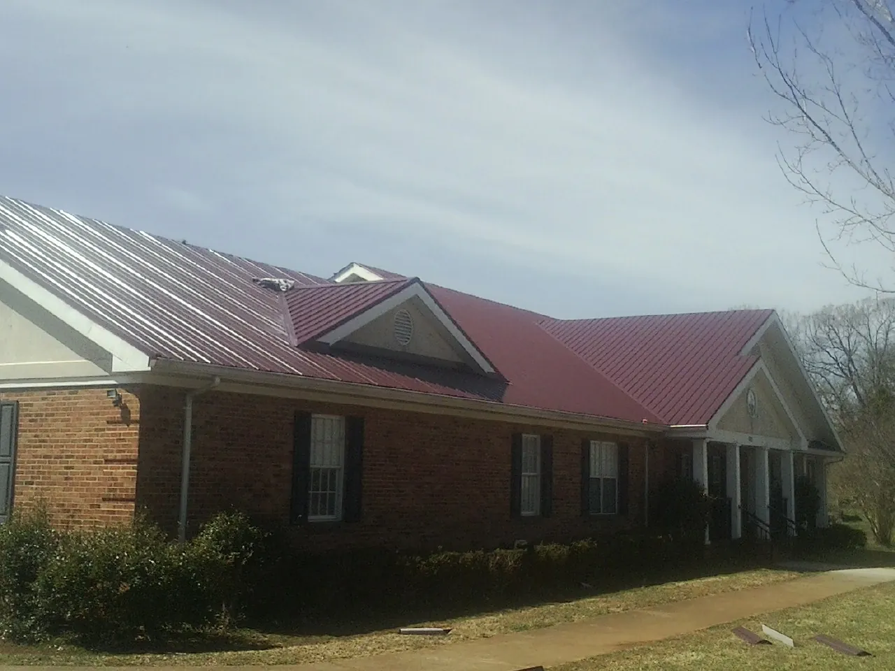 Red metal roof with gabled entries on a long brick building, from a Hail Damage Roof Repair job in Royalston