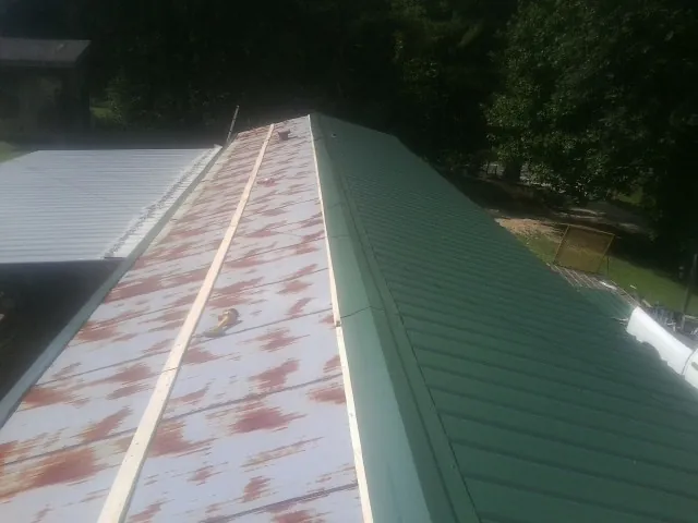 Old rusted panels beside newly installed green metal roofing — Wind Damage Roof Repair by Roofing Brothers in Royalston