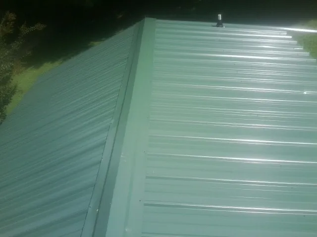 New green metal panels meeting at the ridge of a roof — Flat Roof Repair work by our crew in Royalston