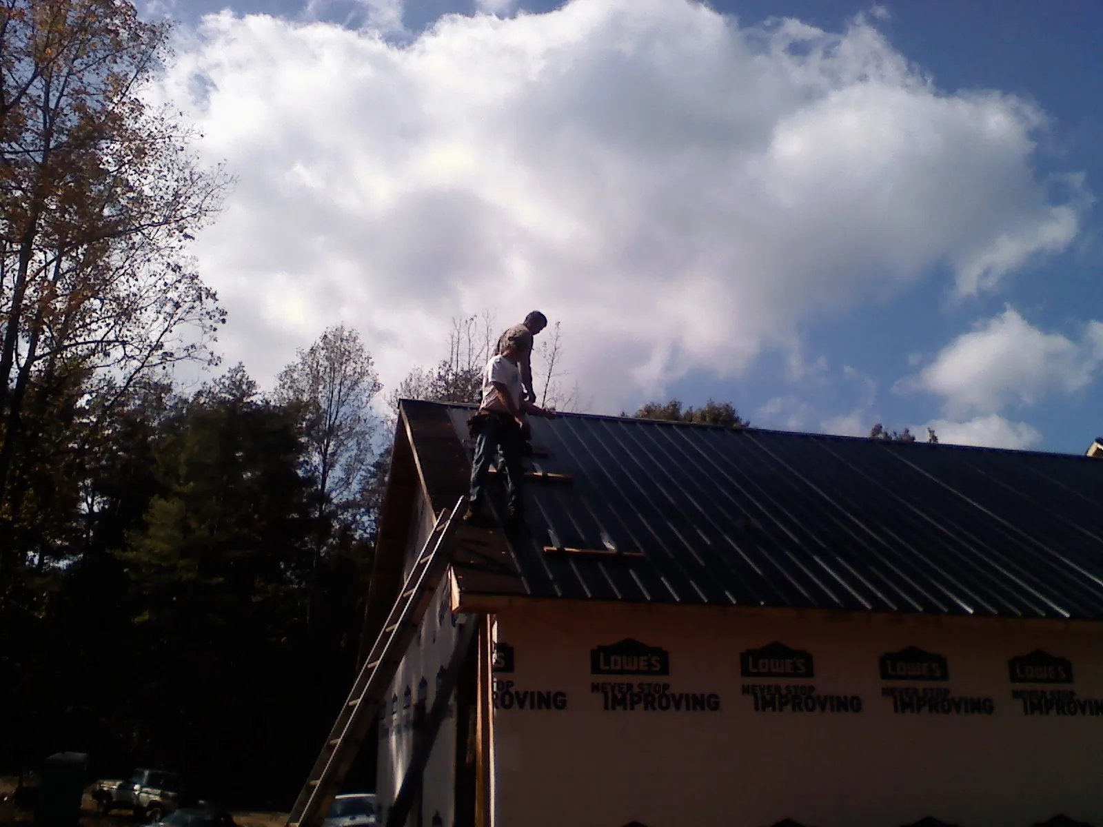 Roofer fastening dark metal panels high against a cloudy sky, from a Roof Inspection job in Royalston