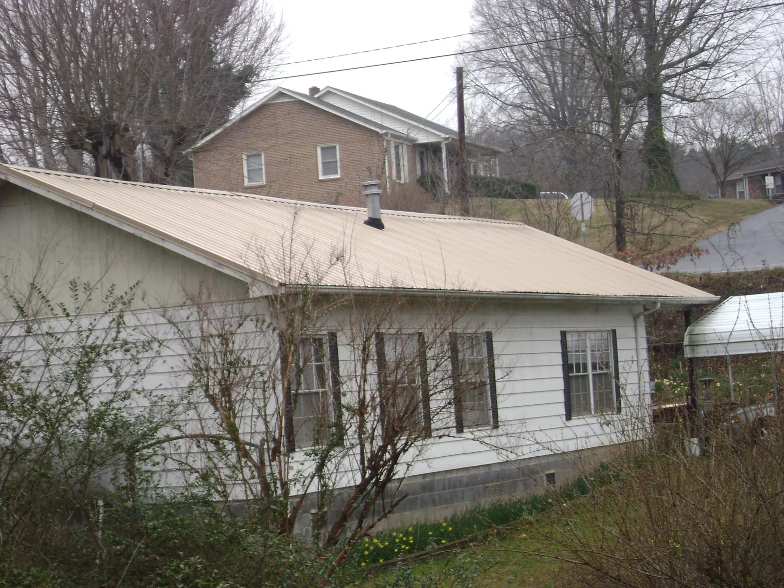 Tan metal roof on a white sided house set into a hillside — Commercial Roofing by Roofing Brothers in Royalston